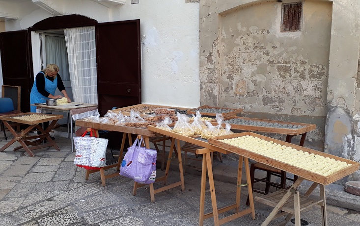 Woman working on the dough for the orecchiette on "pasta street", while the ready pasta is drying.
