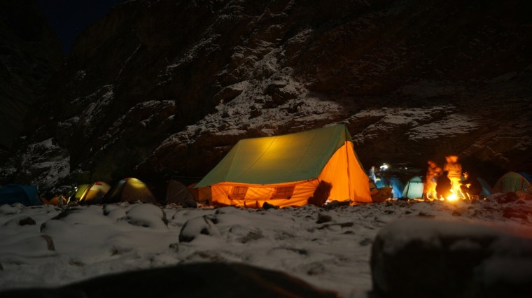 winter camping group around the fire with glowing tents nearby